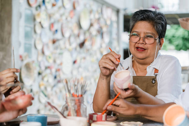 An elderly woman painting a ceramic vessel
